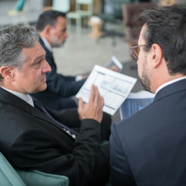 Two businessmen engaged in a discussion, examining reports in a modern office environment.